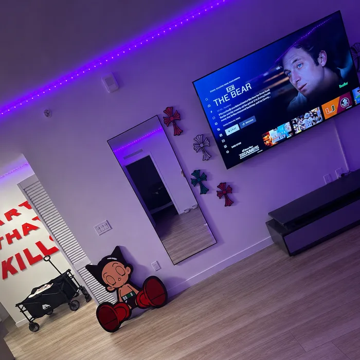 A living room lit purple, with epoxy crosses and a boxing-glove cartoon boy on the wall beside ART THAT KILLS lettering