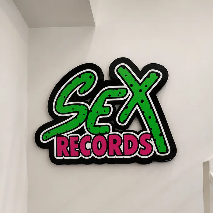 The SEX RECORDS sign at the top of a stairwell, a caped Grover figure standing in the corner beneath it