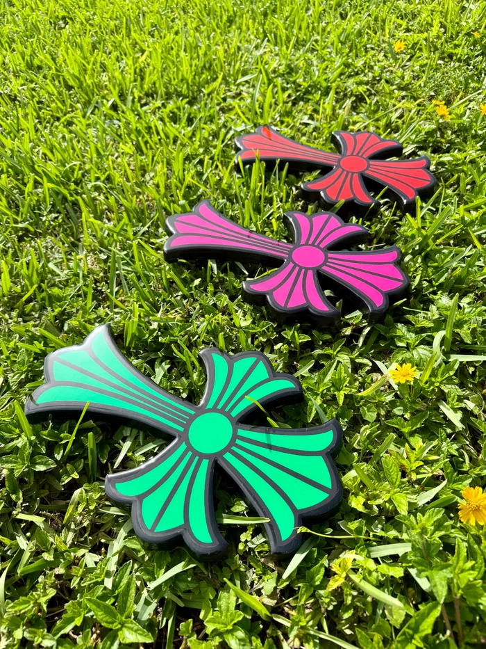 Three glossy epoxy crosses in pink, red and teal lying on grass