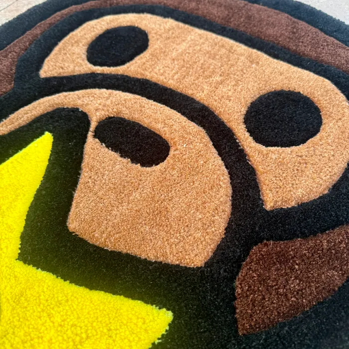 Close detail of a hand-tufted rug — dense brown and yellow yarn pile forming an ape face and star
