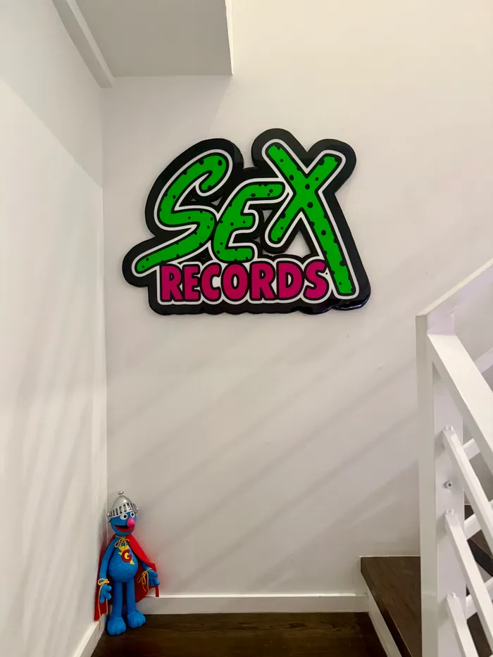 A green and pink glossy epoxy sign reading Sex Records on a white wall