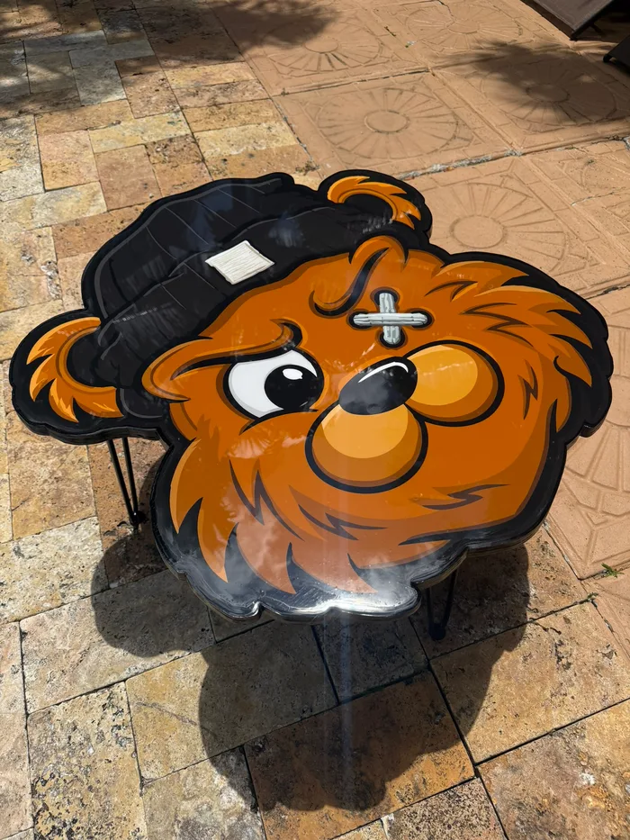 A round epoxy table topped with a cartoon bear face, on black hairpin legs